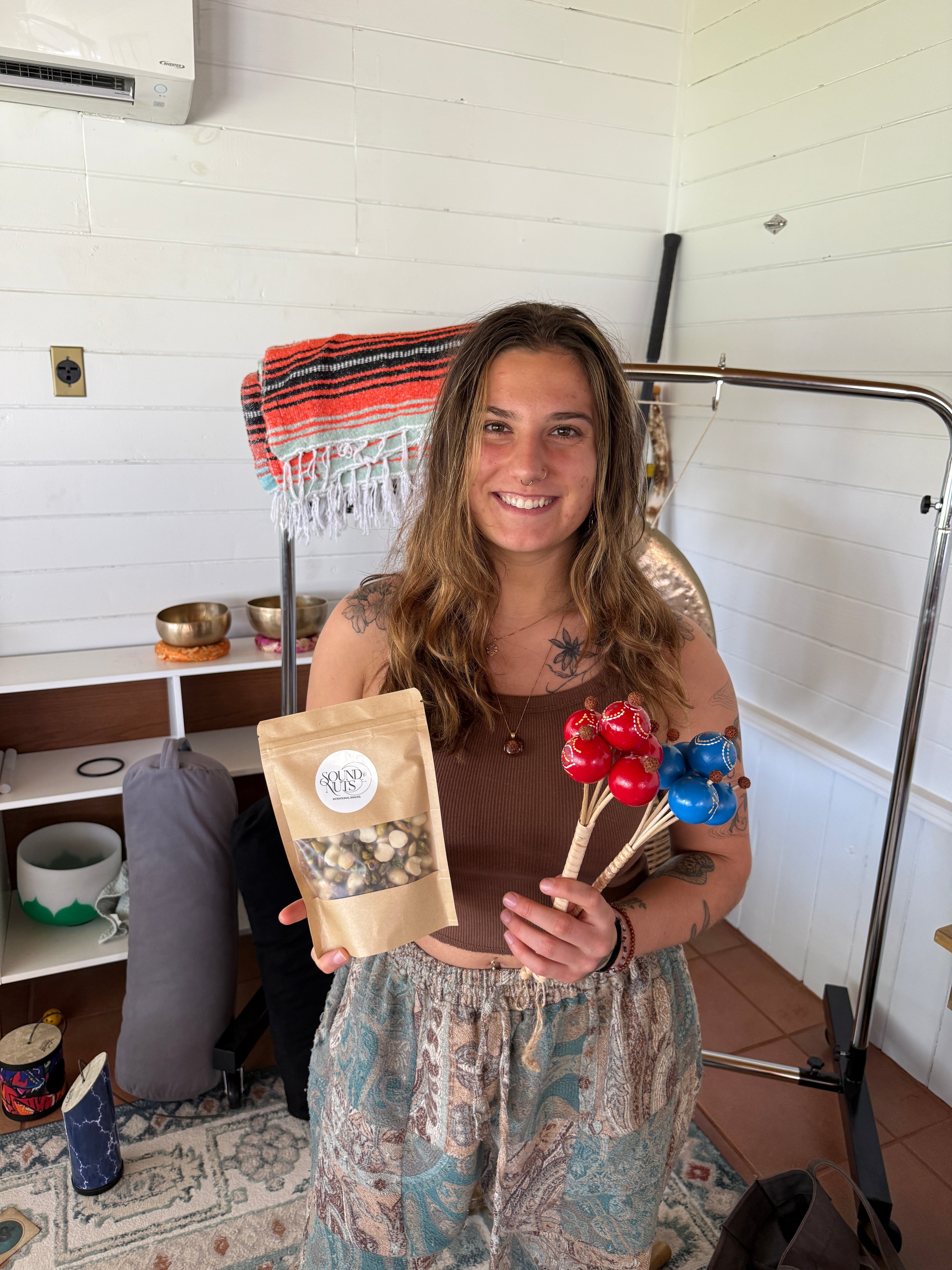 Woman holding a bag of nuts and 2 shakers in a room with a white wall and wooden floor.